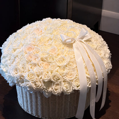 Cream preserved rose basket with long ribbons displayed against a dark interior