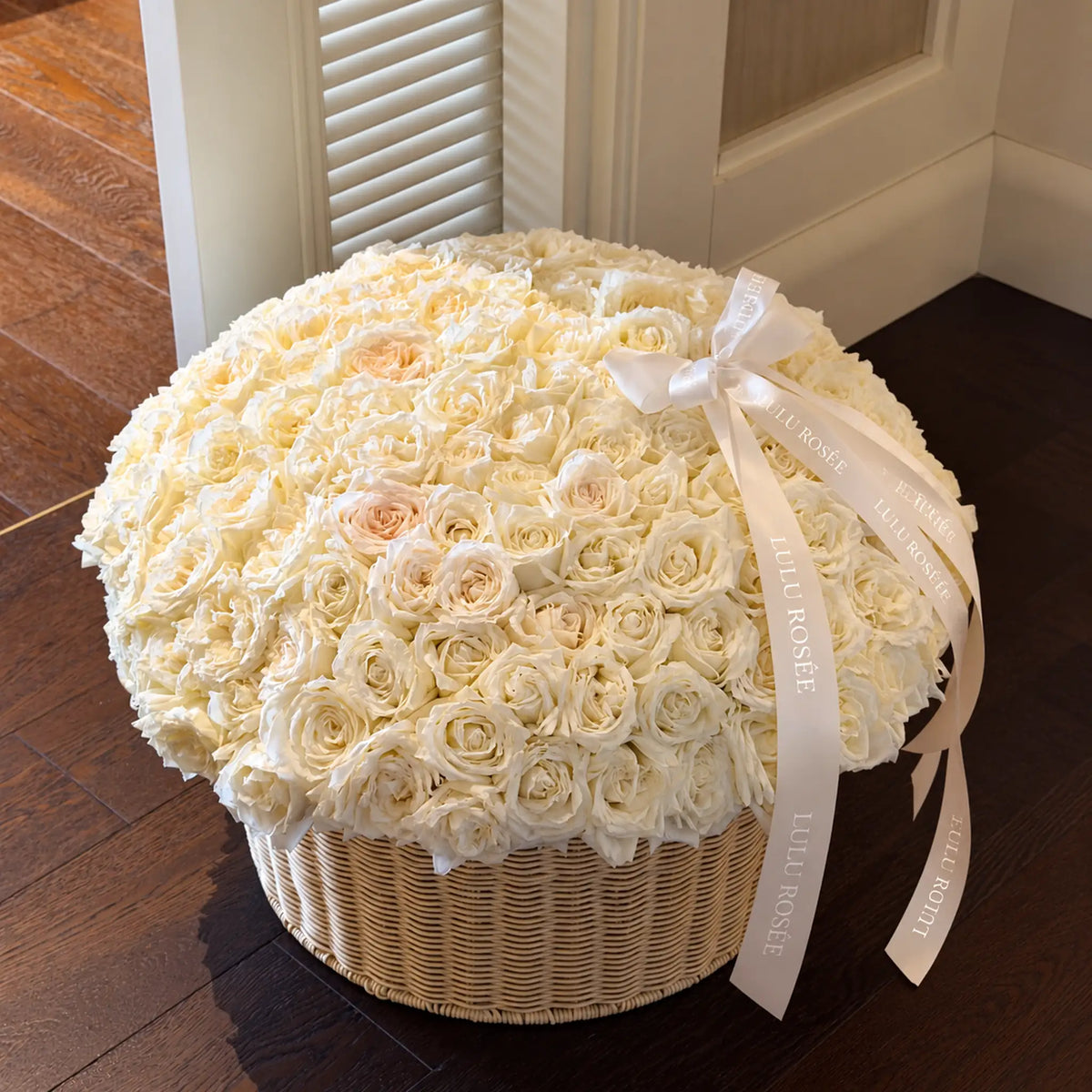 Cream preserved rose basket displayed on a dark wooden floor beside a door