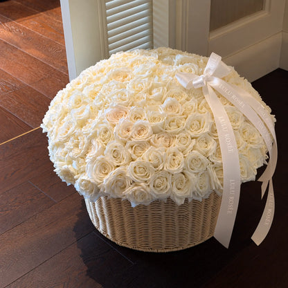 Cream preserved rose arrangement with a white bow and long ribbons in an interior setting