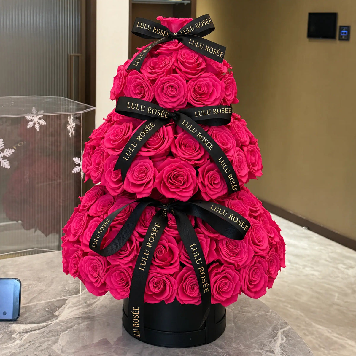 Hot pink preserved rose Christmas tree displayed on a table beside a snowflake display