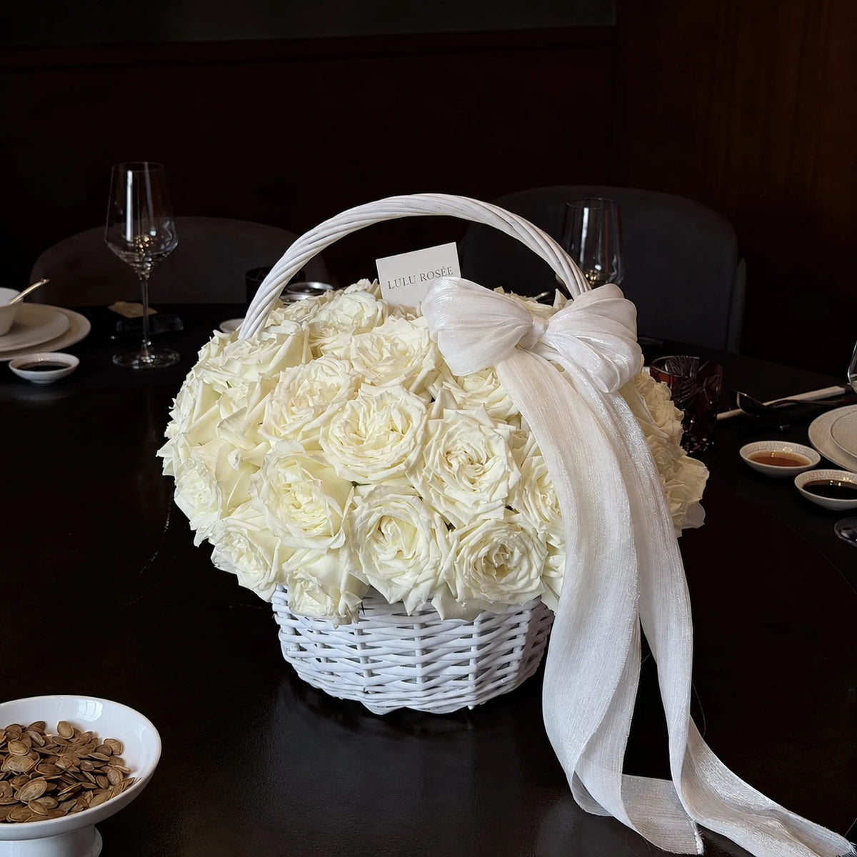 Ivory-toned preserved rose basket shown in a dark dining setting