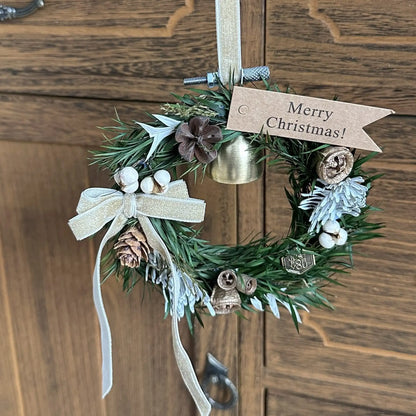 Miniature green Christmas wreath with a gold bell displayed against a wooden door.