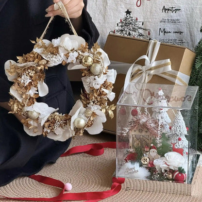 White and gold preserved orchid wreath held beside gift boxes and a separate Christmas village display.