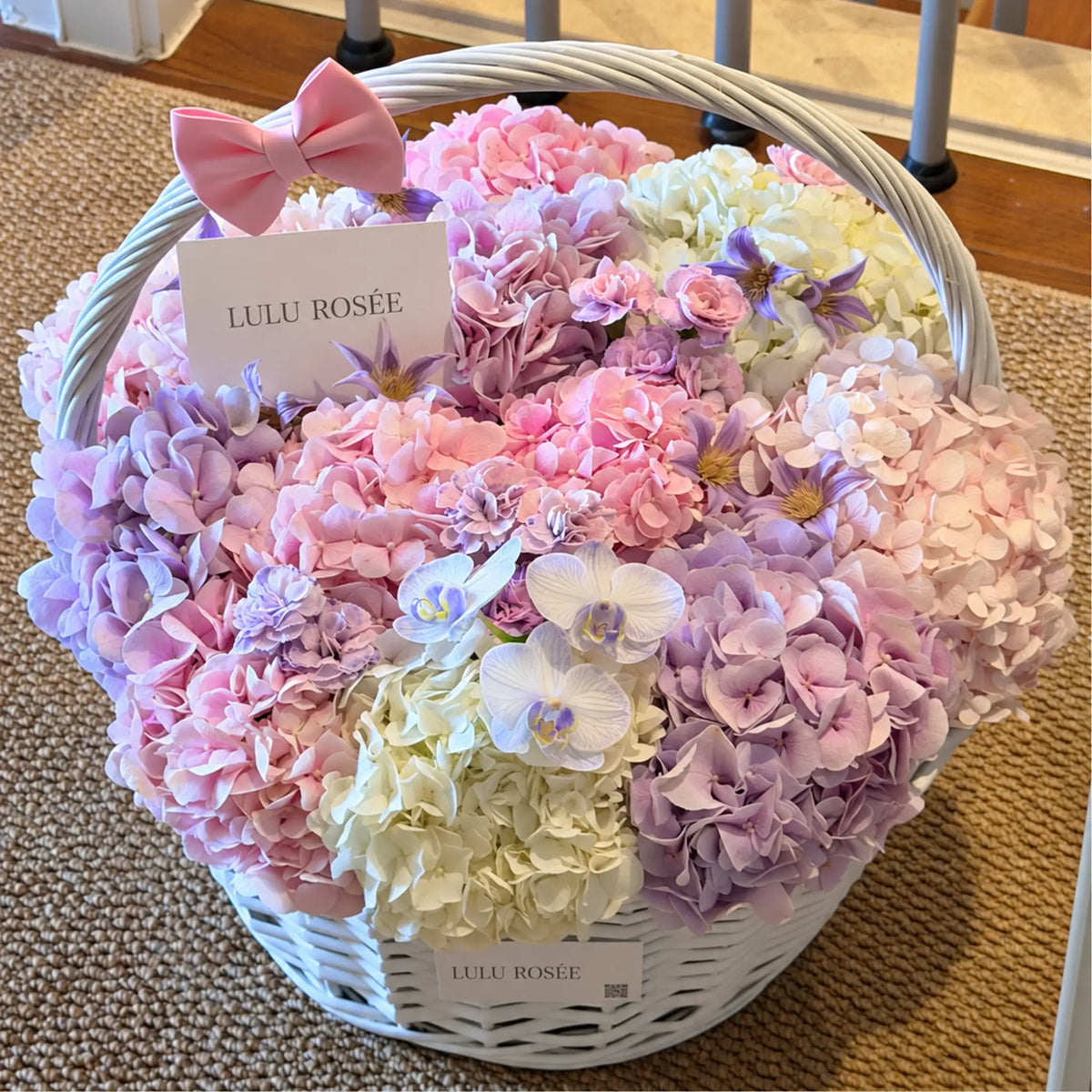 Pink and lavender preserved hydrangeas in a white handled basket with a pink bow