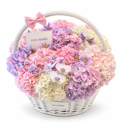Pastel preserved hydrangea basket with white orchids and a pink bow on a white background