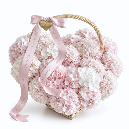 Petite blush preserved hydrangea heart basket with a curved handle and pink ribbons on a white background
