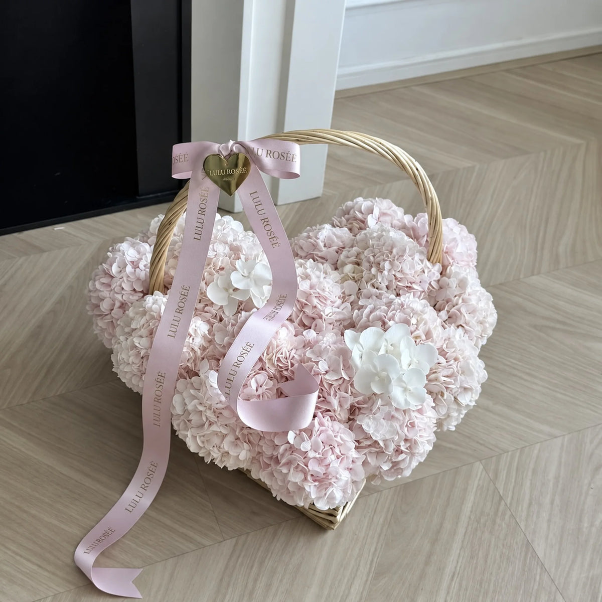 Pink ribbons draped over a petite preserved hydrangea heart basket