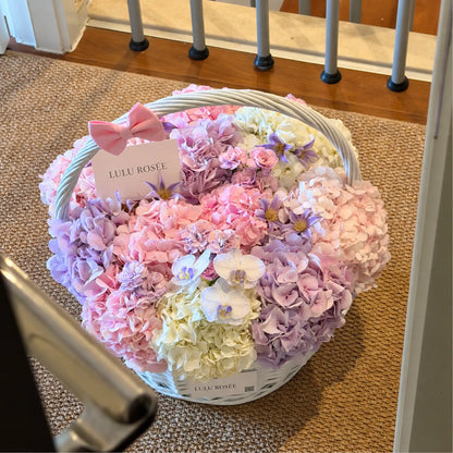 Pastel preserved hydrangea basket with a pink bow shown near a staircase