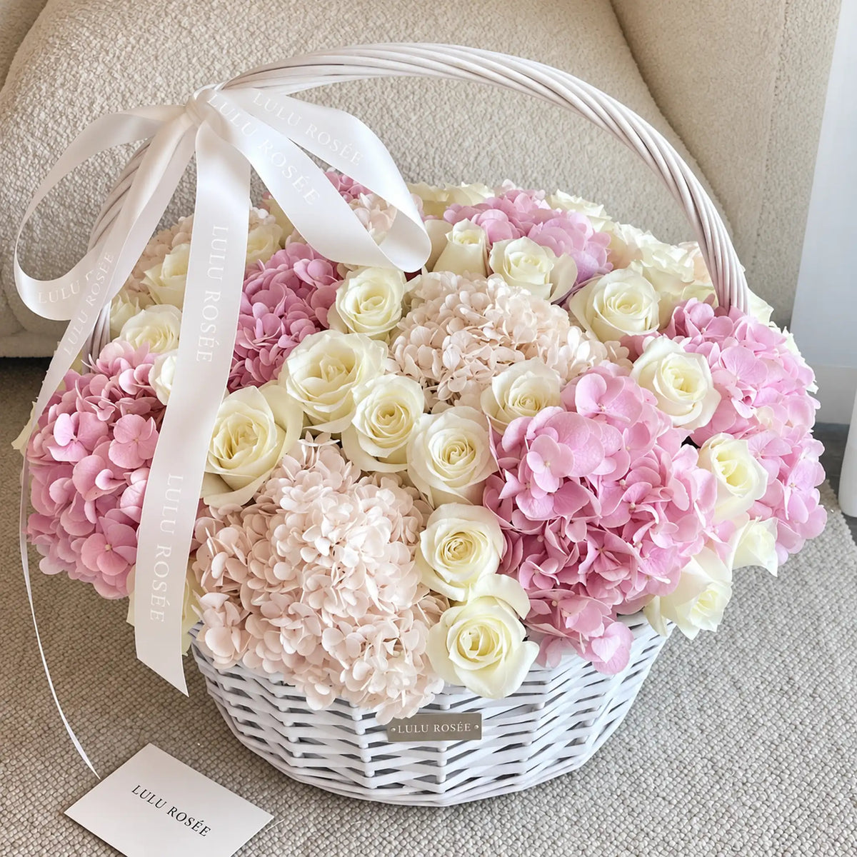 Angled view of a white handled basket filled with preserved roses and blush hydrangeas