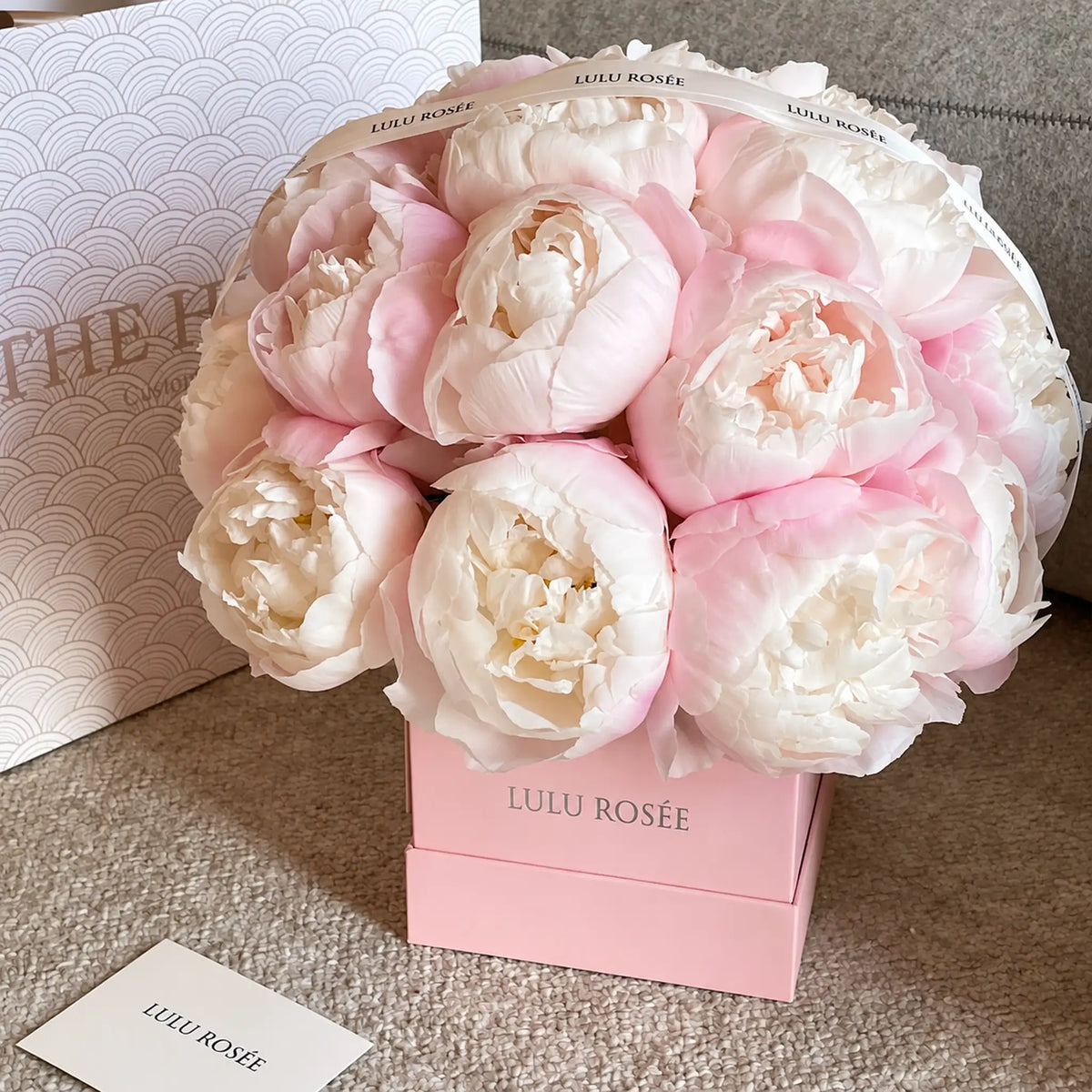 Pink and white preserved peony box displayed beside a LULU ROSÉE card
