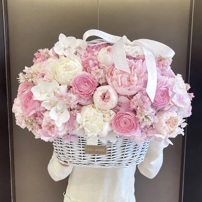 Pink and white preserved flower basket held in front of a dark background