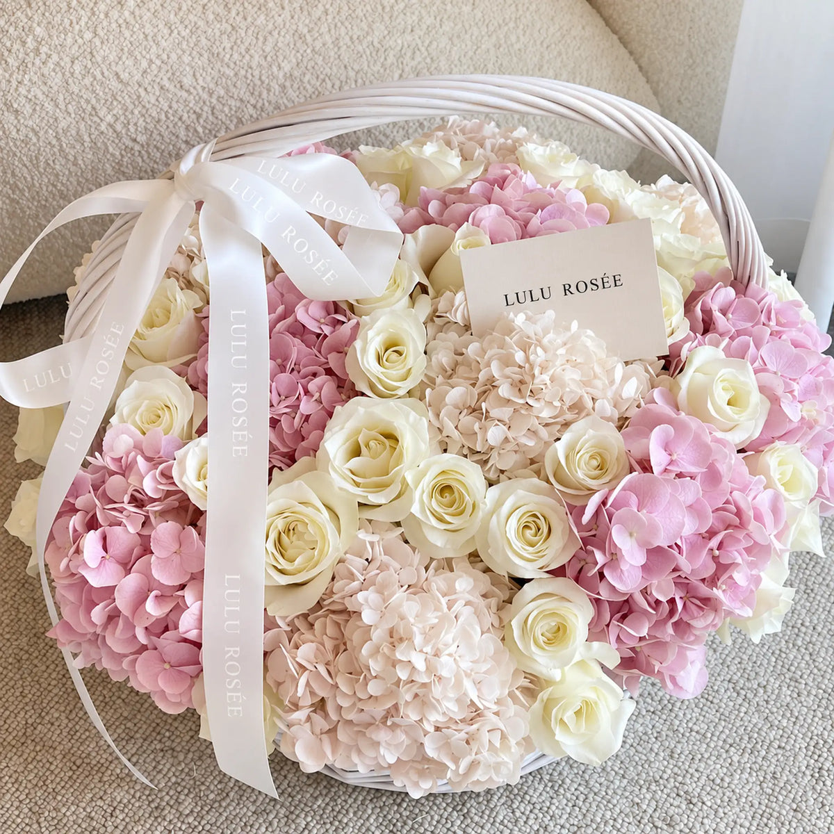 Overhead view of cream preserved roses and pink hydrangeas with a white ribbon