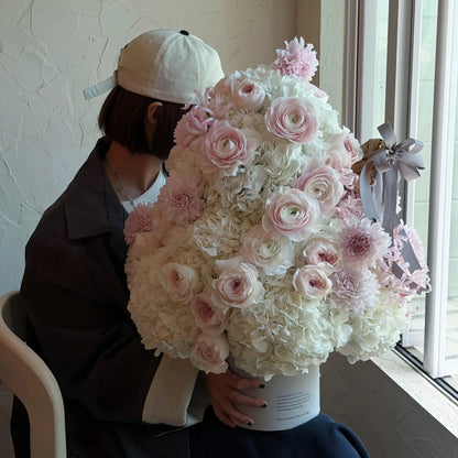 Blush preserved flower tree held beside a window, showing its layered floral form