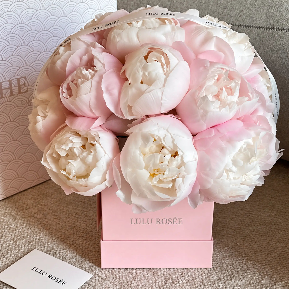 Angled view of a pink square box filled with soft preserved peonies