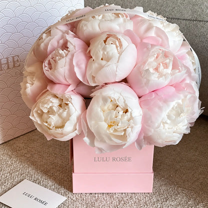 Angled view of a pink square box filled with soft preserved peonies