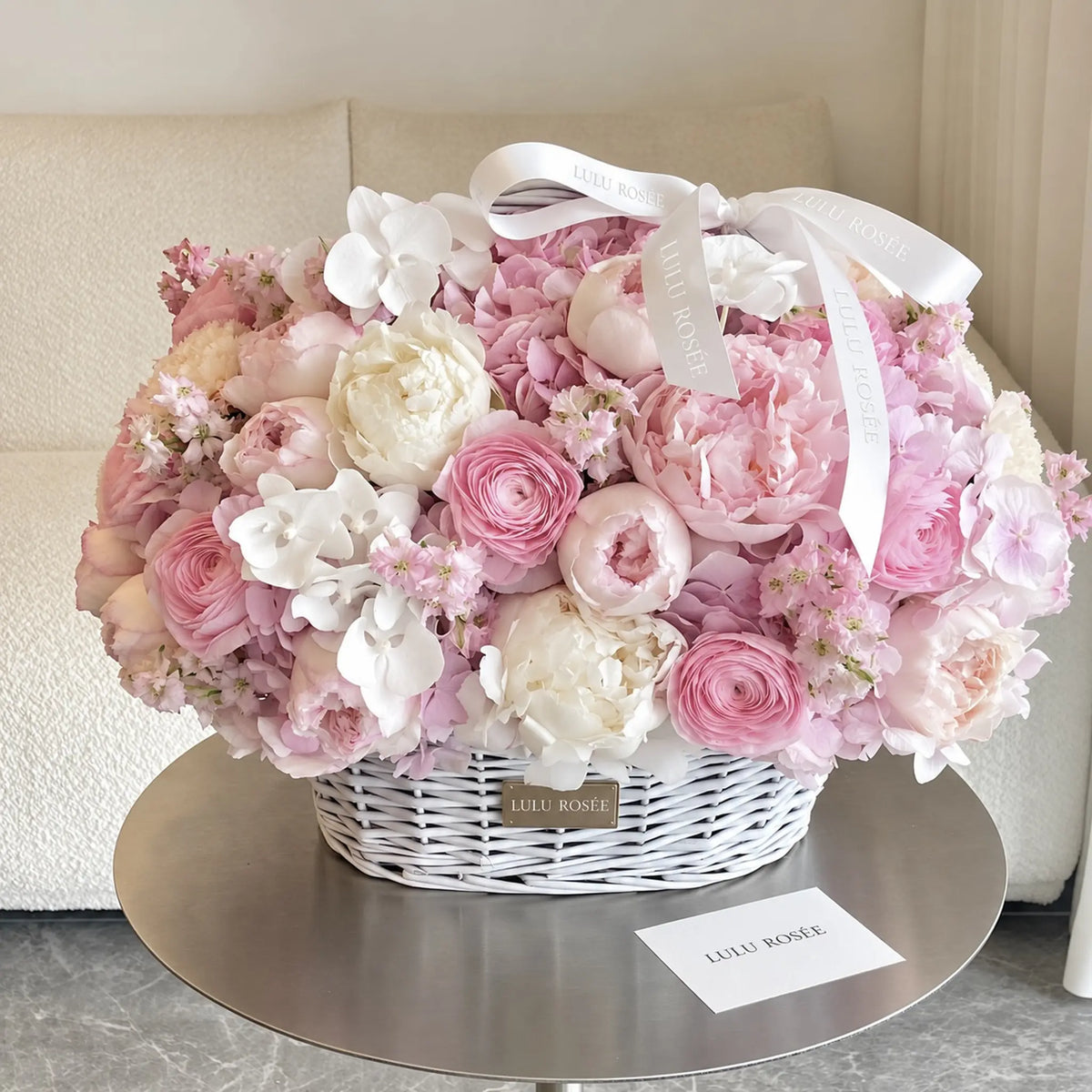 Pink preserved peonies and roses arranged in a white basket with a ribbon