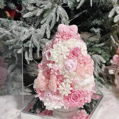 Pink and white preserved flower tree with roses beside snowy evergreen branches.