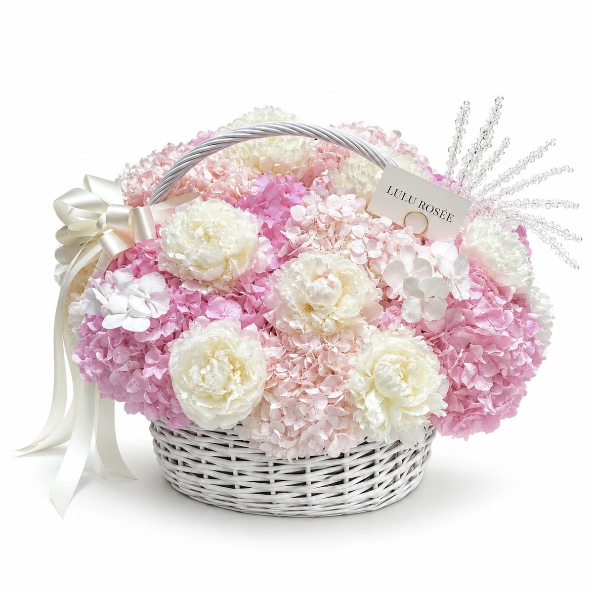 White handled basket of preserved white peonies and pink hydrangeas on a white background