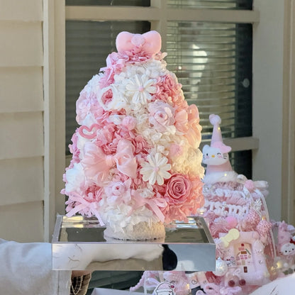 Pink preserved flower Christmas tree displayed beside seasonal decorations.