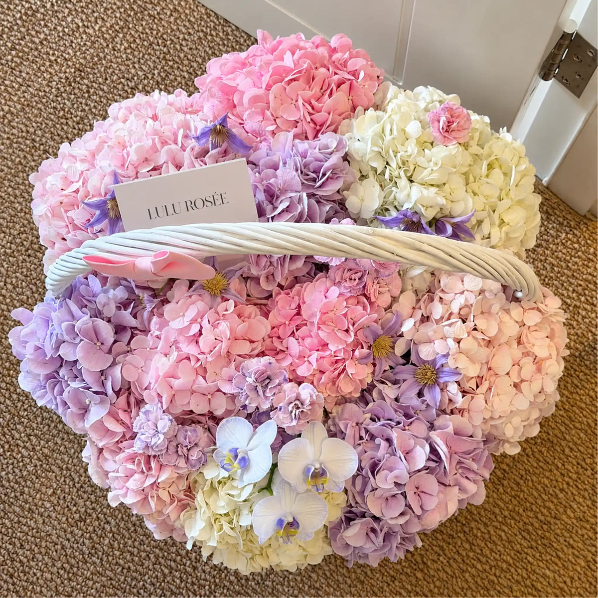 Top view of a pastel preserved flower basket with a LULU ROSÉE card and white handle