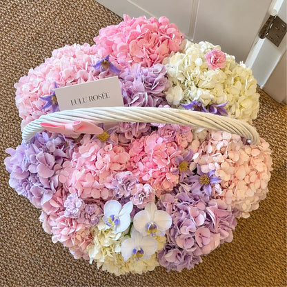 Top view of a pastel preserved flower basket with a LULU ROSÉE card and white handle