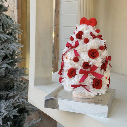 White preserved flower tree with red roses displayed by a window on a mirrored base.