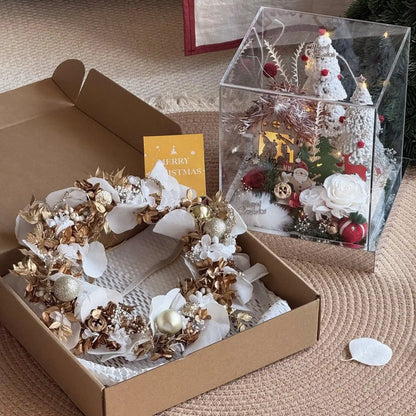 Preserved flower wreath in an open gift box beside a separate Christmas village display.