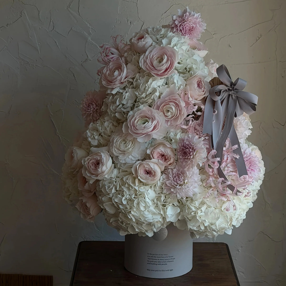 Preserved white hydrangeas and blush flowers arranged as a Christmas tree on a wooden table