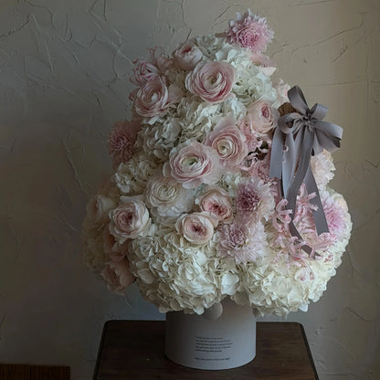 Preserved white hydrangeas and blush flowers arranged as a Christmas tree on a wooden table