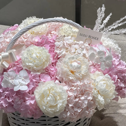 Close view of white preserved peonies among pink and pale hydrangeas in a handled basket