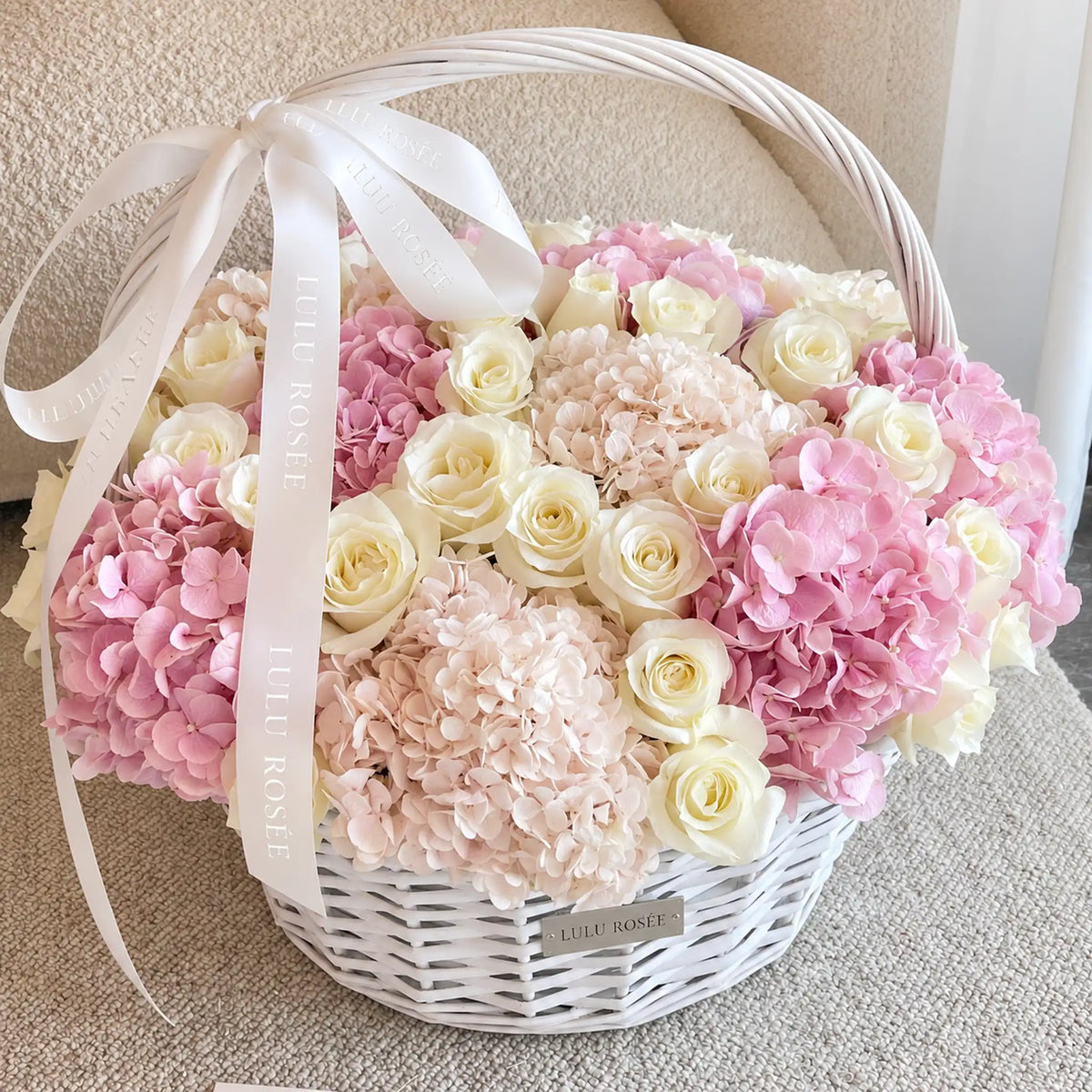 Preserved cream roses and pink hydrangeas in a white basket with a ribbon bow
