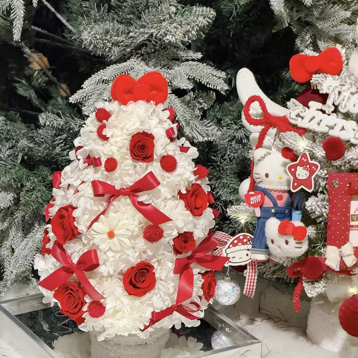 Christmas tree arrangement of white preserved hydrangeas and red roses beside seasonal decorations.