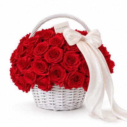 Red preserved roses in a white handled basket with a white bow