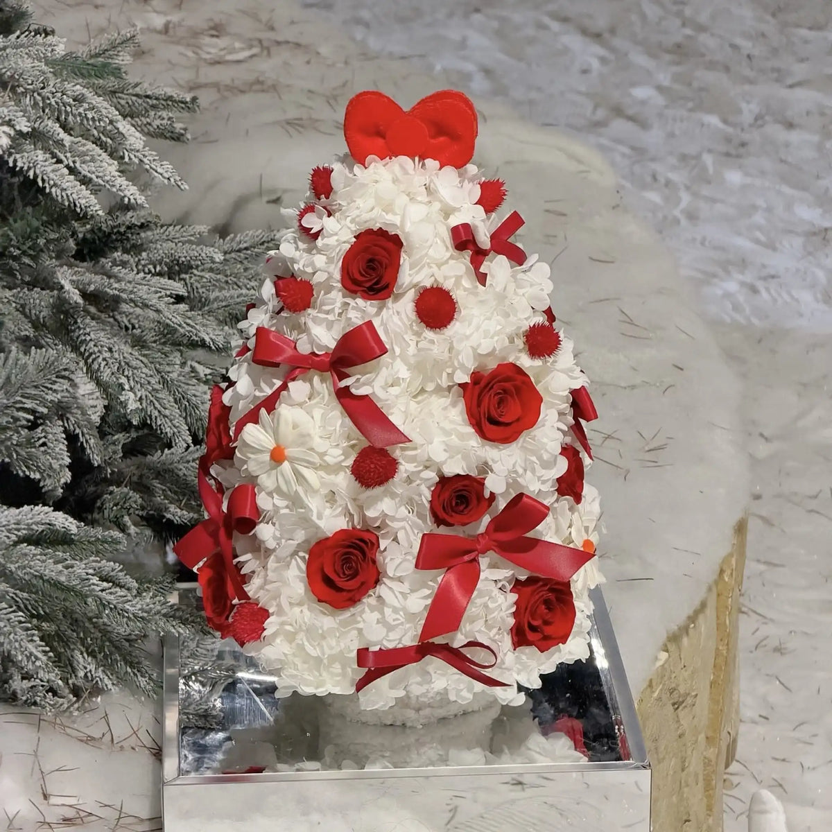 Red preserved roses and ribbon bows accent a white hydrangea Christmas tree in a festive setting.