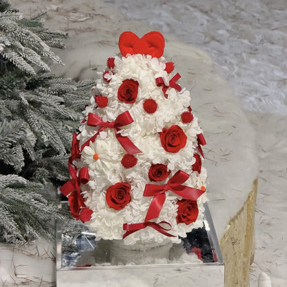 Red preserved roses and ribbon bows accent a white hydrangea Christmas tree in a festive setting.