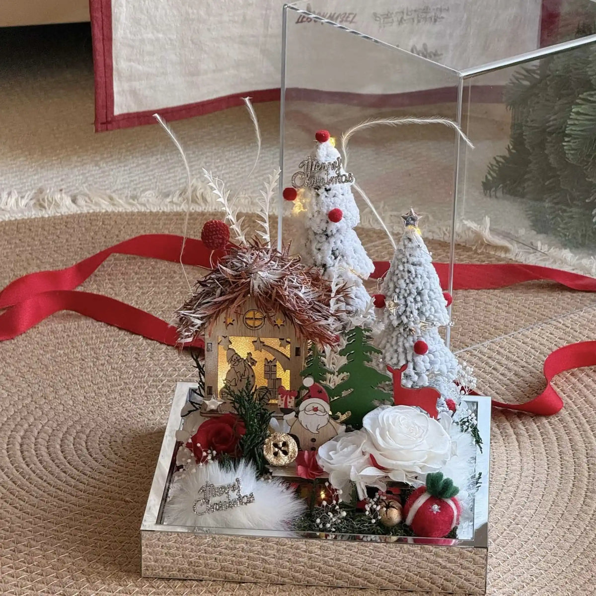 Front view of a winter cottage display with preserved roses and miniature snow-covered trees.
