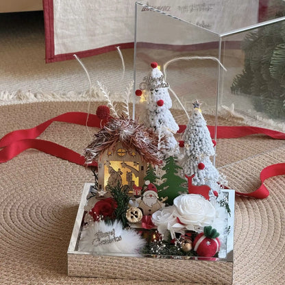 Front view of a winter cottage display with preserved roses and miniature snow-covered trees.