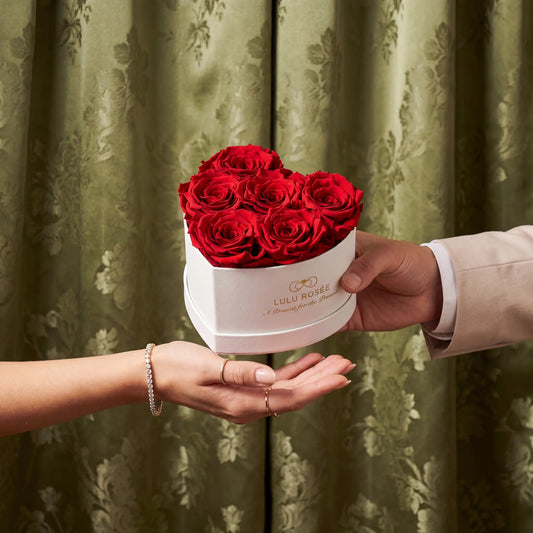 Person holding a white box with red roses against a green curtain background
